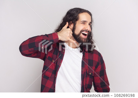 Give me call sometimes. Cheerful smiling man with long curly hair shapes hand like phone, looks gladfully aside, asks for telephone number. Indoor studio shot isolated on gray background. Give me call sometimes. Cheerful smiling man with long curly hair shapes hand like phone, looks gladfully aside, asks for telephone number. Indoor studio shot isolated on gray background. 108269198
