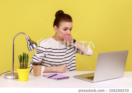 portrait of shocked woman office worker covering mouth, looking at laptop screen with terrified expression, found scary secret. Indoor studio studio shot isolated on yellow background. 108269250