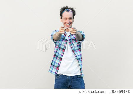 You got it. I choose you and order. Man in casual blue checkered shirt and headband points at camera with index fingers picks someone smiles broadly. Indoor studio shot isolated on gray background. You got it. I choose you and order. Man in casual blue checkered shirt and headband points at camera with index fingers picks someone smiles broadly. Indoor studio shot isolated on gray background. 108269428