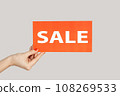 Closeup of woman hand showing card with sale inscription, special offer, shopping discounts. Indoor studio shot isolated on gray background. 108269533