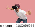 Portrait of amazed wary bearded man in white T-shirt and beany hat, wearing vr, playing in headset, trying to avoid monster in video game. Indoor studio shot isolated on pink background. 108269544