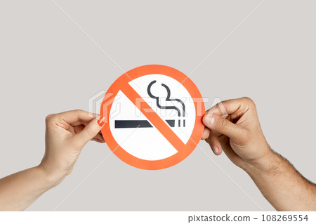 Closeup of woman hands showing card with no smoking sign, healthy lifestyle, healthy habits. Indoor studio shot isolated on gray background. 108269554