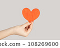 I love you. Closeup of woman hand showing little red paper heart symbol of love and devotion. Indoor studio shot isolated on gray background. 108269600