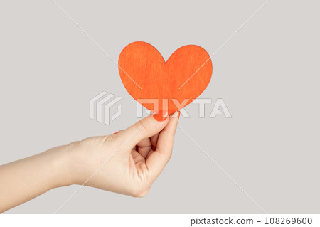 I love you. Closeup of woman hand showing little red paper heart symbol of love and devotion. Indoor studio shot isolated on gray background. 108269600