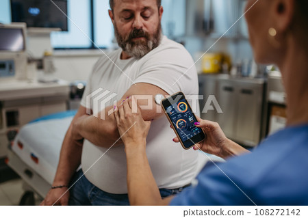 Doctor connecting continuous glucose monitor with smartphone, to check blood sugar level in real time. Obese, overweight man is at risk of developing type 2 diabetes. Concept of health risks of 108272142