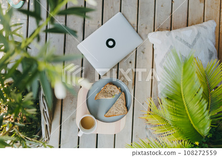 Top view of outdoor garden patio setting with notebook, plate with light lunch and cup of coffee. Simple outdoor home office for remote employee, telecommuter. 108272559