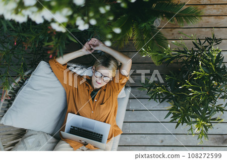 Top view of woman working outdoors in the garden, with laptop on legs. Businesswoman working remotely from homeoffice, thinking about new business or creative idea. Concept of outdoor home office. Top view of woman working outdoors in the garden, with laptop on legs. Businesswoman working remotely from homeoffice, thinking about new business or creative idea. Concept of outdoor home office. 108272599