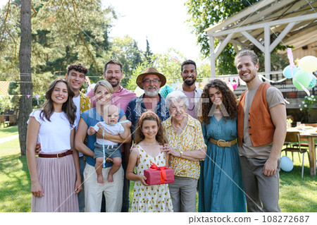 Family portrait at outdoor summer garden party. Family and friends standing, posing for a group photo. Multigenerational family. 108272687