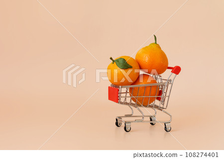 Small shopping cart with tangerines on beige background. Online shopping, fresh fruit delivery concept with copy space. Black Friday, Cyber Monday Sales. Christmas supermarket offers 108274401