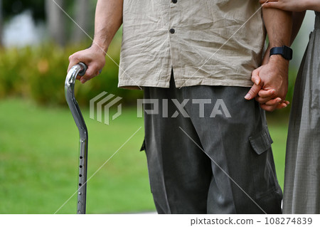 Cropped image of senior man walking with a cane in the park with young adult daughter Cropped image of senior man walking with a cane in the park with young adult daughter 108274839