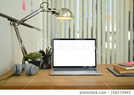 Front view of laptop computer with white screen, headphone, book and lamp on wooden table Front view of laptop computer with white screen, headphone, book and lamp on wooden table 108274945