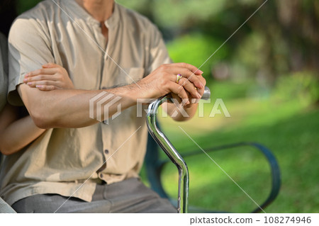 Adult daughter holding hand of middle age father on cane or walking stick showing love and support Adult daughter holding hand of middle age father on cane or walking stick showing love and support 108274946