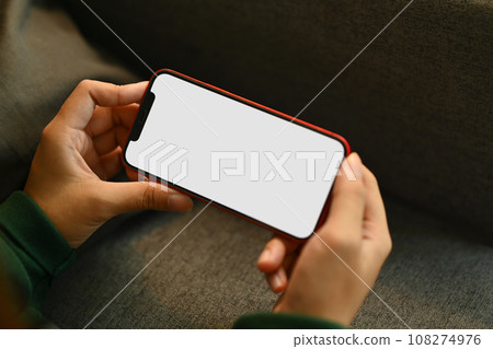 Young woman relaxing on couch holding smartphone watching videos or playing video games at home 108274976