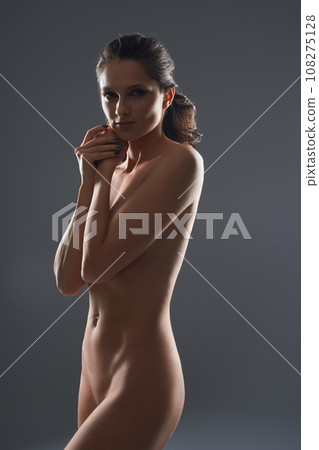 Tender naked woman covering her breast with arms in studio 108275128