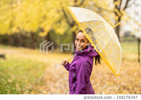 Portrait of a young smiling woman under an umbrella on a walk in the autumn park 108276347