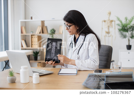 Doctor discussing x-ray with patient on laptop in cabinet 108276367