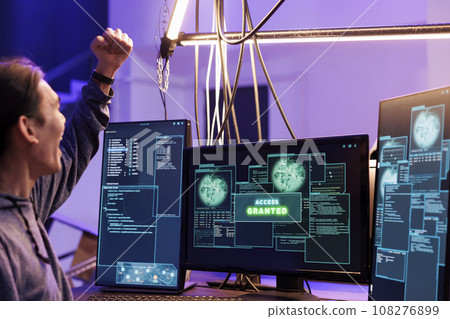 Hacker celebrating access granted to computer system and doing illegal activities. Young asian man raising fist in victory gesture after hacking database successfully in abandoned warehouse 108276899
