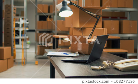 Empty warehouse with office space to work on inventory and logistics, storage room filled with stacks of cardboard boxes on shelves. Storehouse space with racks, quality control on merchandise. 108277156