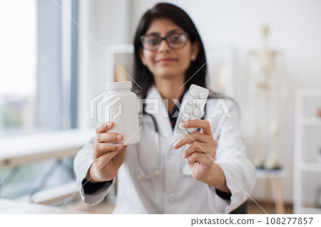 Indian therapist showing white pills while sitting at desk 108277857