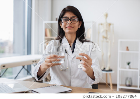 Woman doctor holding glass of water and pills in hands 108277864