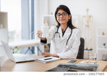 Female family doctor showing oral medication in jar at desk Female family doctor showing oral medication in jar at desk 108277885