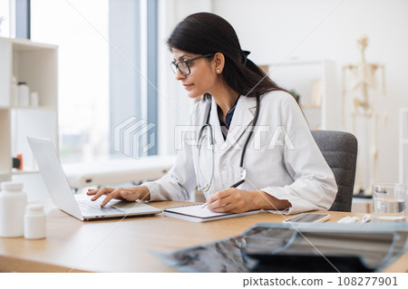 Doctor using computer while sitting at desk in health center Doctor using computer while sitting at desk in health center 108277901