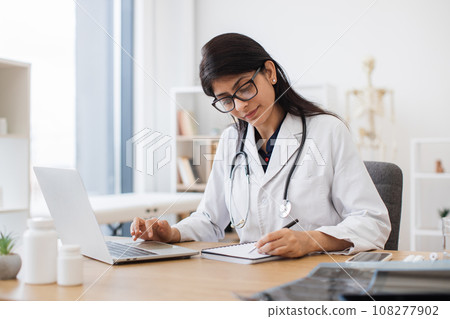Doctor using computer while sitting at desk in health center Doctor using computer while sitting at desk in health center 108277902