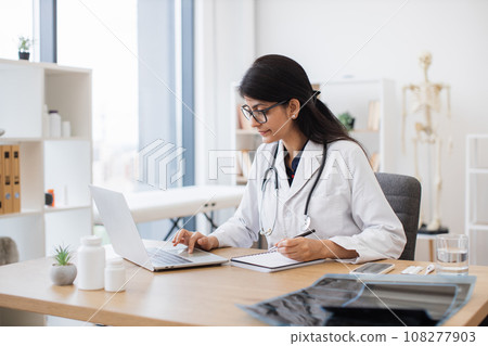Doctor using computer while sitting at desk in health center 108277903