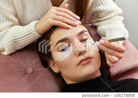cosmetologist removes glue cotton tape under eye. Eyelash extension procedure cosmetologist removes glue cotton tape under eye. Eyelash extension procedure 108278008