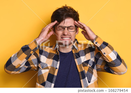 Stressed man in glasses has headache against yellow studio wall 108279454