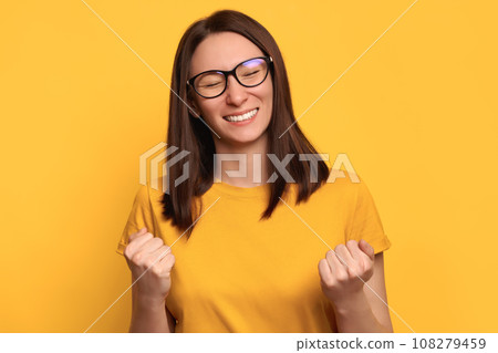 Beautiful girl celebrating and doing winner gesture on yellow background 108279459