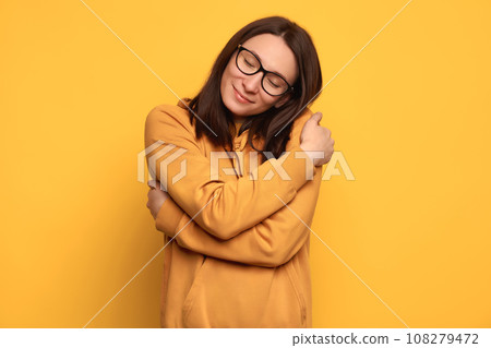 Beautiful happy girl with good self esteem hugging herself on yellow background 108279472