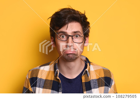 Offended young guy looking at camera isolated on yellow studio wall Offended young guy looking at camera isolated on yellow studio wall 108279505