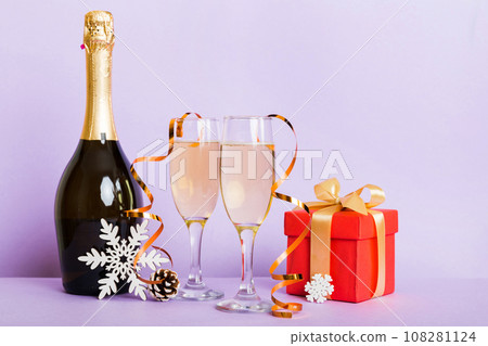 Champagne bottle with confetti, glasses and christmas decor on colored holiday background. Flat lay New Year decorations Champagne bottle with confetti, glasses and christmas decor on colored holiday background. Flat lay New Year decorations 108281124