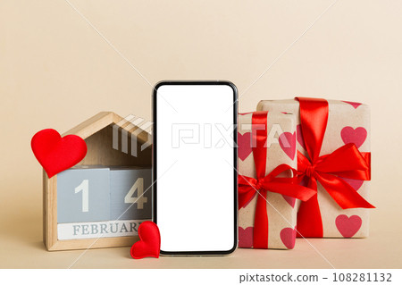mobile phone with blank screen on colored background with hearts, calendar and gift box, valentine day 14 february concept perspertive view flat lay mobile phone with blank screen on colored background with hearts, calendar and gift box, valentine day 14 february concept perspertive view flat lay 108281132