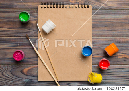 Album pages and paints, pencils, brush on a colored background. Top view with empty space. workplace for creativity. home teaching concept drawing Album pages and paints, pencils, brush on a colored background. Top view with empty space. workplace for creativity. home teaching concept drawing 108281371