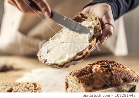 A woman makes delicious bread, spreads cream cheese with a cutlery knife - Close up. Woman hands spreading cream cheese on bread slice. A woman makes delicious bread, spreads cream cheese with a cutlery knife - Close up. Woman hands spreading cream cheese on bread slice. 108281442