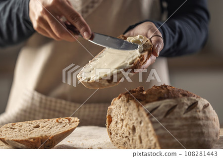 A woman makes delicious bread, spreads cream cheese with a cutlery knife - Close up. Woman hands spreading cream cheese on bread slice. 108281443