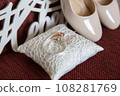 Elegant white bridal heels and wedding ring on a reflective surface, with a luxuriously blurred room backdrop. 108281769