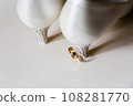 Elegant white bridal heels and wedding ring on a reflective surface, with a luxuriously blurred room backdrop. 108281770