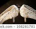 Elegant white bridal heels and wedding ring on a reflective surface, with a luxuriously blurred room backdrop. 108281781