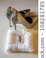 Elegant white bridal heels and wedding ring on a reflective surface, with a luxuriously blurred room backdrop. 108281785