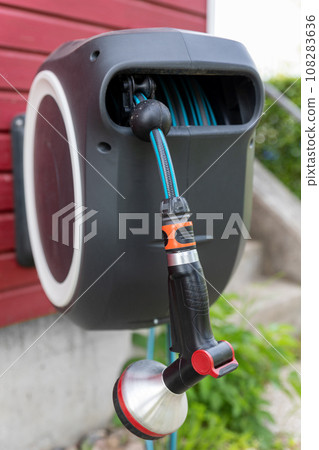 Wall Mounted Retractable Hose Reel. Modern garden lawn watering tip hose with sprinkler hanged at home wall. Lawn and plant tree smart irrigation water system equipment tool Wall Mounted Retractable Hose Reel. Modern garden lawn watering tip hose with sprinkler hanged at home wall. Lawn and plant tree smart irrigation water system equipment tool 108283636