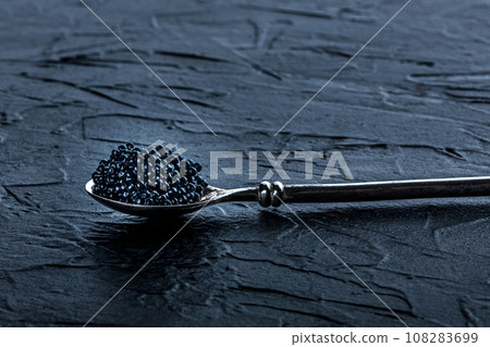 A silver spoon with black caviar on a dark slate background 108283699