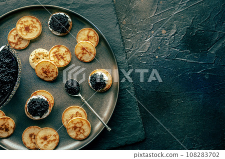 Blinis with black caviar and cream cheese, overhead flat lay shot on black 108283702