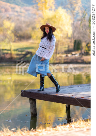 Autumn lake woman. She stands by a pond on a wooden pier in autumn and admires nature. The concept of tourism, weekends outside the city. 108284277