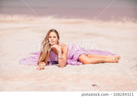 A woman in a pink dress lies on the shore of a pink lake, takes a photo for memory and leaves unforgettable memories. A woman in a pink dress lies on the shore of a pink lake, takes a photo for memory and leaves unforgettable memories. 108284321