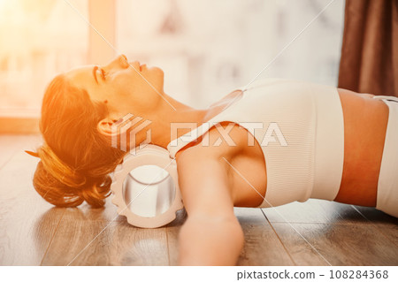 Adult athletic woman, in white bodysuit, performing fascia exercises on the floor - caucasian woman using a massage foam roller - a tool to relieve tension in the back and relieve muscle pain - the Adult athletic woman, in white bodysuit, performing fascia exercises on the floor - caucasian woman using a massage foam roller - a tool to relieve tension in the back and relieve muscle pain - the 108284368