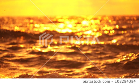 Blurred golden sea at sunset. The sun reflects and sparkles on the waves with bokeh, illuminating the golden sea. Holiday recreation concept. Abstract nautical summer ocean sunset nature background 108284384