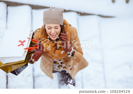 smiling stylish woman in brown hat and scarf talking on phone 108284529